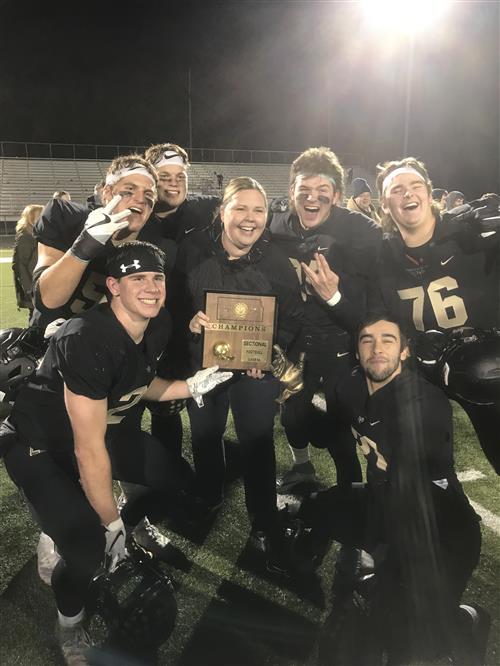 Image of teacher surrounded by six students after their football game